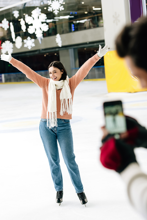 selective focus of man taking photo of excited woman on smartphone on skating rink