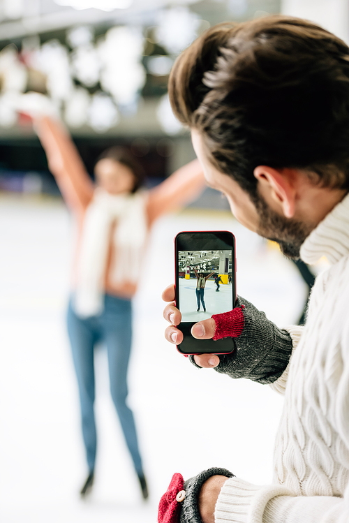 selective focus of handsome man taking photo of excited woman on smartphone on skating rink