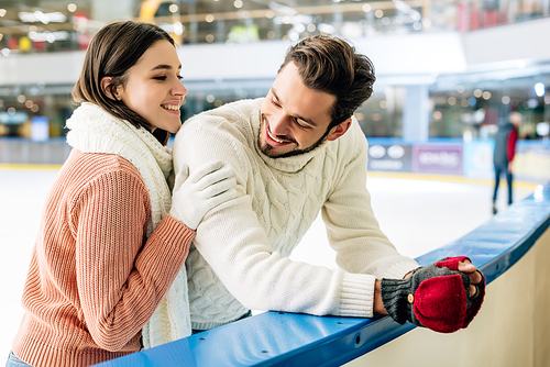 cheerful young couple in sweaters spending time on skating rink