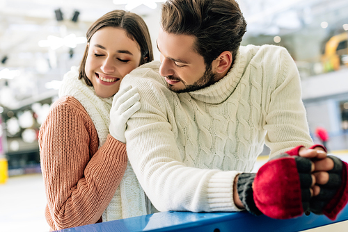 beautiful cheerful couple in sweaters spending time on skating rink