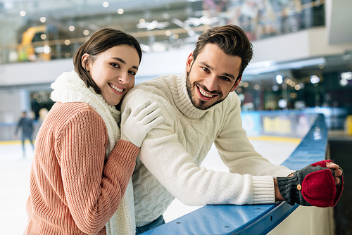 young positive couple in sweaters spending time on skating rink