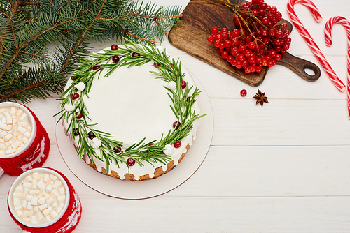 top view of christmas pie on white wooden table with candy canes, cocoa, viburnum berries and spruce branches