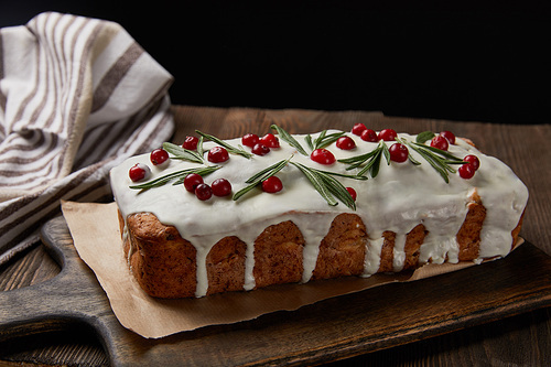 traditional Christmas cake with cranberry and rosemary on wooden table isolated on black