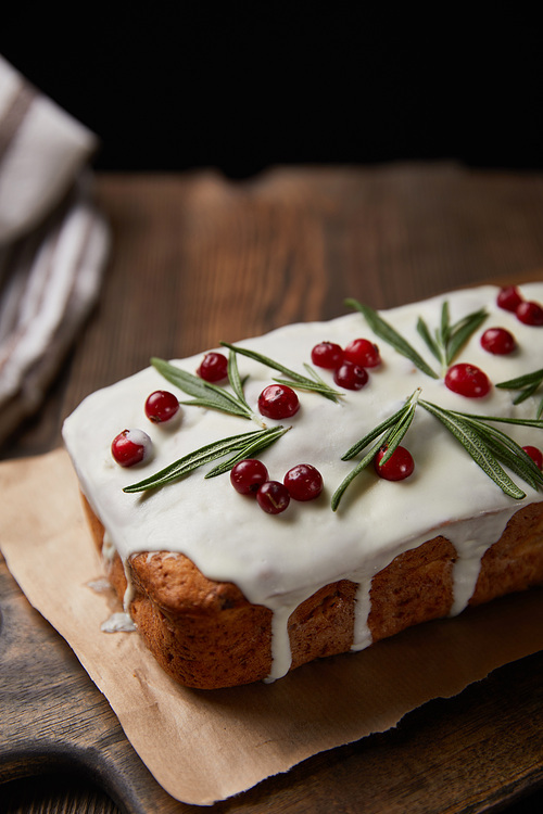 close up view of traditional Christmas cake with cranberry and rosemary on wooden table isolated on black