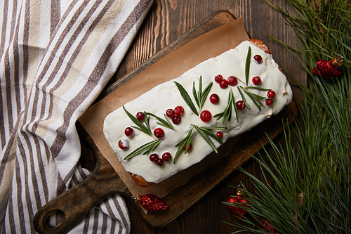 top view of traditional Christmas cake with cranberry near pine branch with red baubles and napkin on wooden table