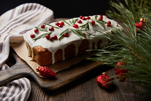 traditional Christmas cake with cranberry near pine branch with red baubles and napkin on wooden table isolated on black
