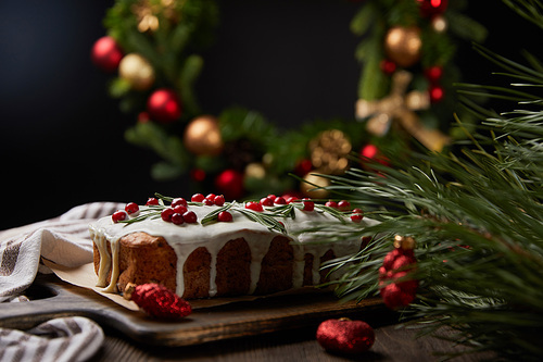 selective focus of traditional Christmas cake with cranberry near Christmas wreath with baubles on wooden table isolated on black