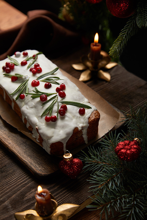 traditional Christmas cake with cranberry near pine with baubles and candles on wooden table