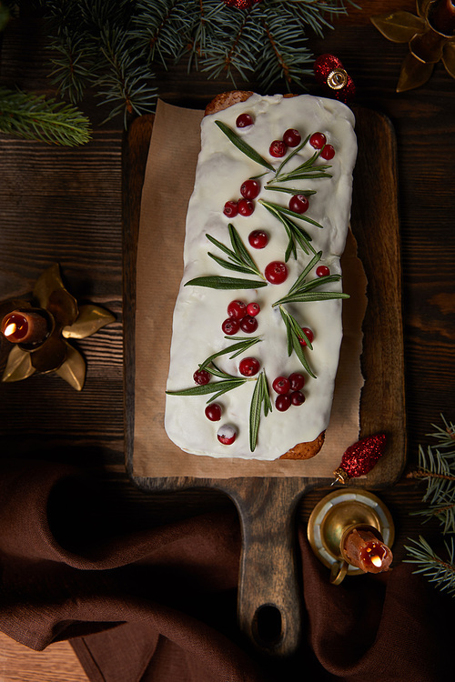 top view of traditional Christmas cake with cranberry near pine and candles on wooden table