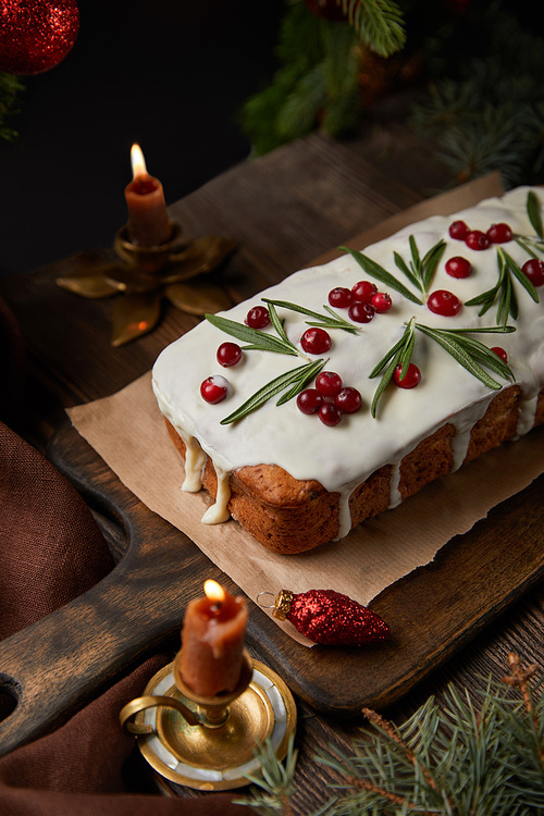 traditional Christmas cake with cranberry near pine and candles on wooden table
