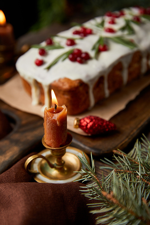 selective focus of traditional Christmas cake with cranberry near burning candle on wooden table