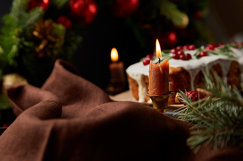 selective focus of traditional Christmas cake with cranberry near burning candles on wooden table