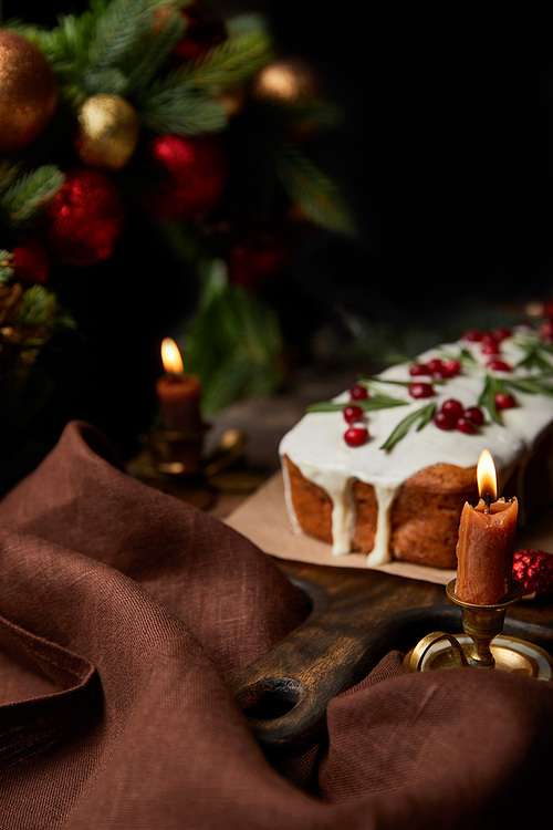 selective focus of traditional Christmas cake with cranberry near burning candles on wooden table