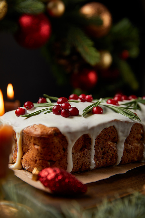 selective focus of traditional Christmas cake with cranberry near burning candles, Christmas wreath with baubles on wooden table