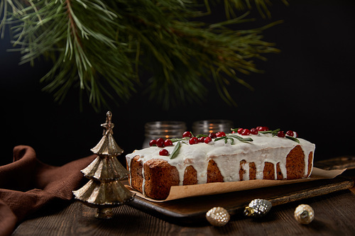 traditional Christmas cake with cranberry near pine, baubles and candles on wooden table