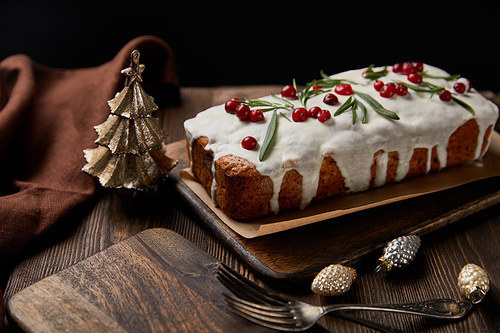 traditional Christmas cake with cranberry near baubles, forks and brown napkin on wooden table isolated on black