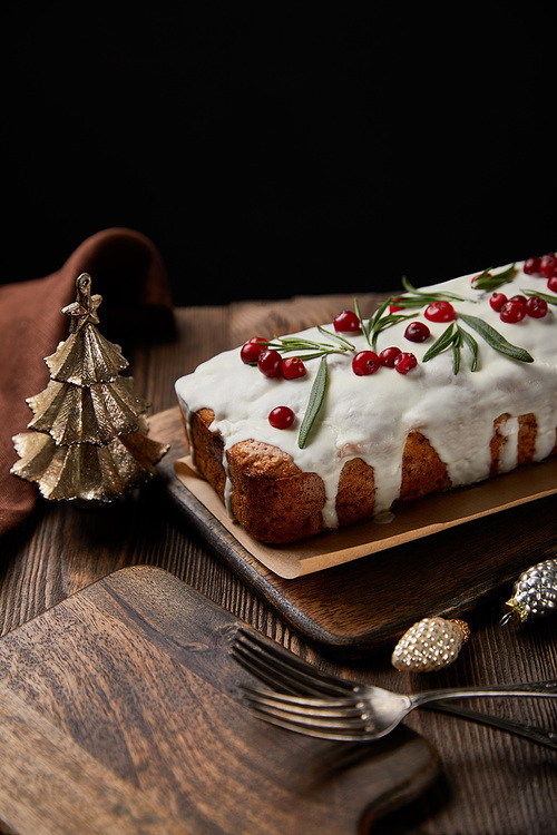 traditional Christmas cake with cranberry near baubles, forks and brown napkin on wooden table isolated on black