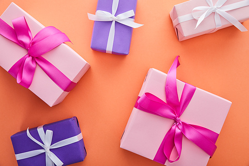 top view of pink and purple gift boxes with ribbons and bows on orange background