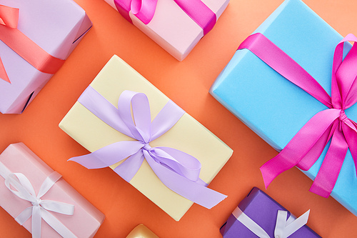 flat lay with multicolored gift boxes with ribbons and bows on orange background