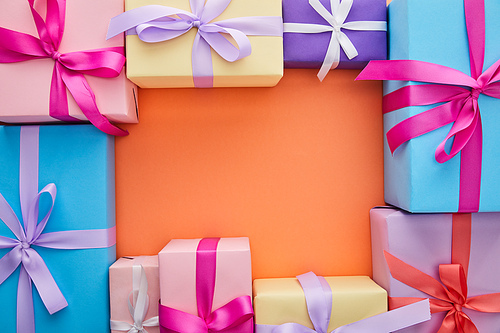square frame of multicolored gift boxes with ribbons and bows on orange background with copy space