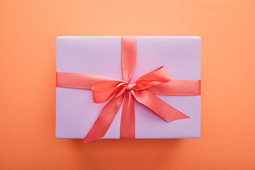 top view of violet gift box with red ribbon and bow on orange background