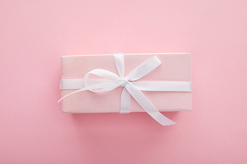 top view of pink gift with white ribbon on pink background