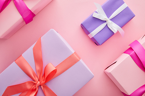 flat lay with colorful gift boxes with ribbons and bows scattered on pink background