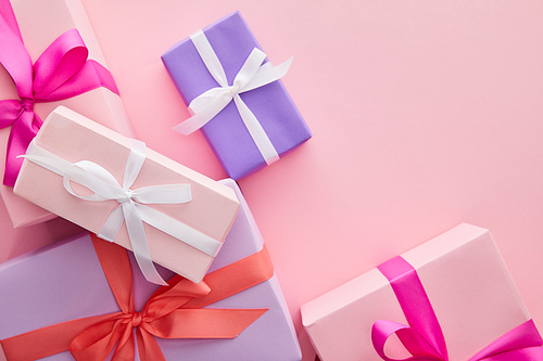 top view of colorful gift boxes with ribbons and bows scattered on pink background