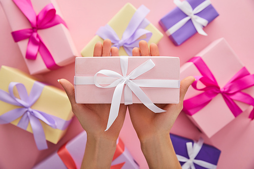cropped view of woman holding pink gift above presents