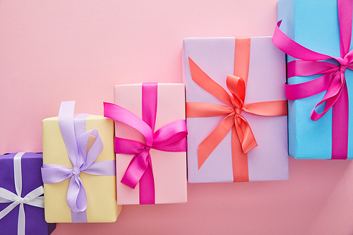 flat lay with colorful gift boxes with ribbons and bows scattered on pink background with copy space