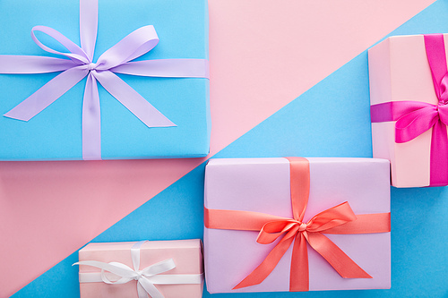 top view of colorful gift boxes with ribbons and bows on blue and pink background