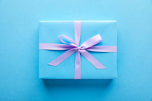 top view of blue gift with violet ribbon on blue background