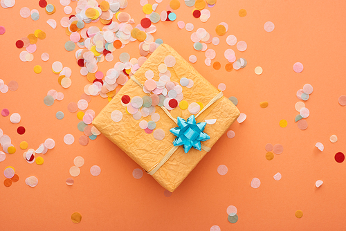top view of gift box with blue bow near confetti on orange