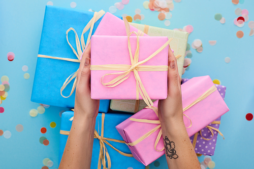 cropped view of woman holding pink gift box near colorful presents near confetti on blue