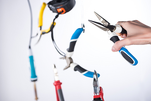 Cropped view of man holding pliers with levitating tools in air isolated on grey
