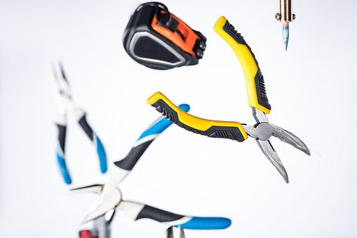 Selective focus of pliers, soldering iron and measuring tape levitating in air isolated on white