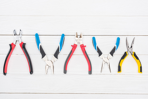 Top view of line of pliers on white wooden background