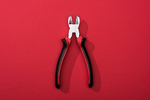 Top view of pliers with shadow on red surface