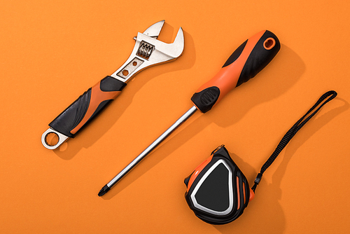 Top view of wrench, screwdriver and measuring tape on orange background