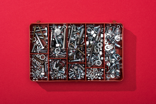 Top view of metal nuts and wood screws in tool box on red background