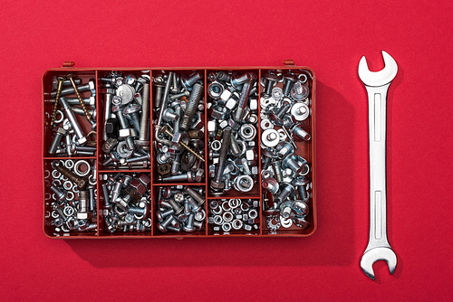 Top view of toolbox with nuts and bolts near wrench on red background