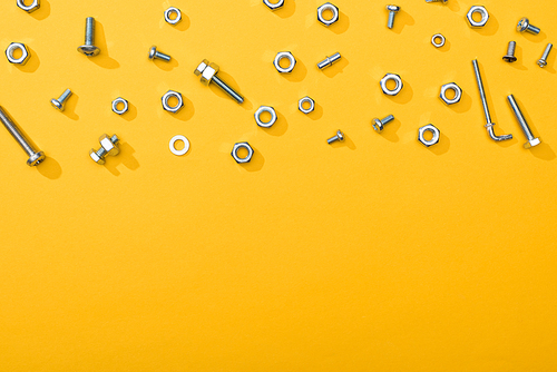Top view of metal nuts and bolts on yellow background with copy space