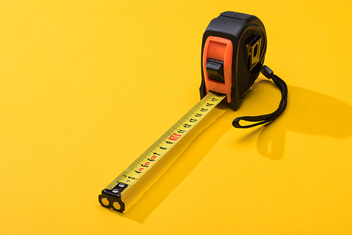 Industrial measuring tape with shadow on yellow background