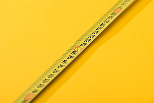 Close up view of numbers on industrial measuring tape on yellow background