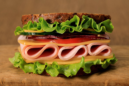 fresh sandwich with lettuce, ham, cheese, bacon and tomato on wooden cutting board