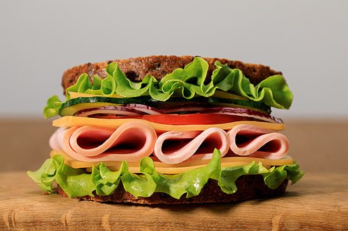 fresh sandwich with lettuce, ham, cheese, bacon and tomato on wooden cutting board isolated on grey