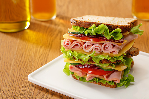 selective focus of fresh sandwich with lettuce, ham, cheese, bacon and tomato near bottles of beer at wooden table