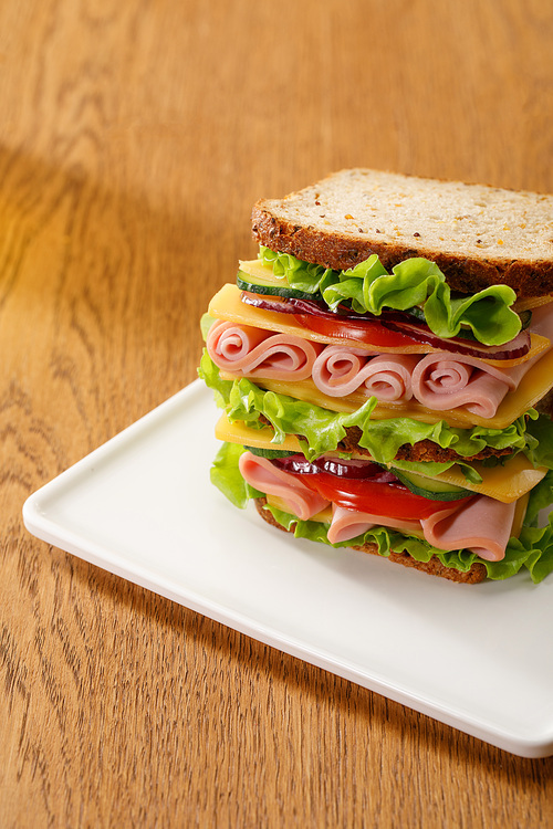 fresh sandwich with lettuce, ham, cheese, bacon and tomato at wooden table