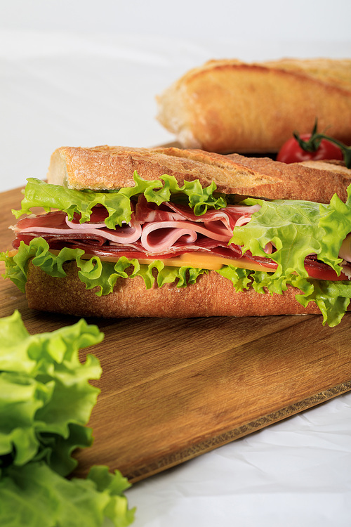 selective focus of fresh sandwich with lettuce, ham, cheese, bacon and tomato on wooden cutting board