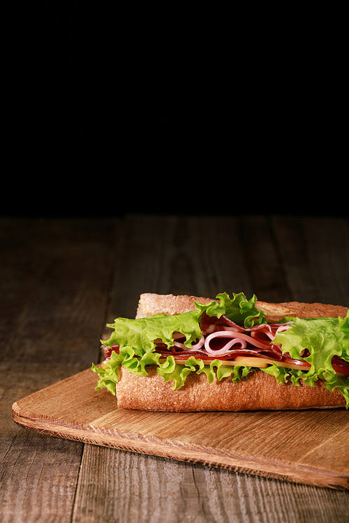 fresh sandwich with lettuce, ham, cheese, bacon and tomato on wooden cutting board isolated on black